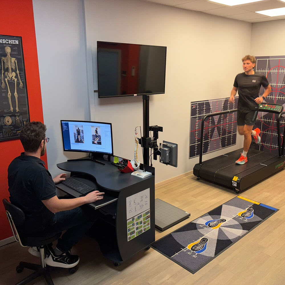 Übersicht eines Analyse­raums mit Laufband, Monitoren und Fachpersonal, das die Laufbewegung eines Sportlers auswertet
