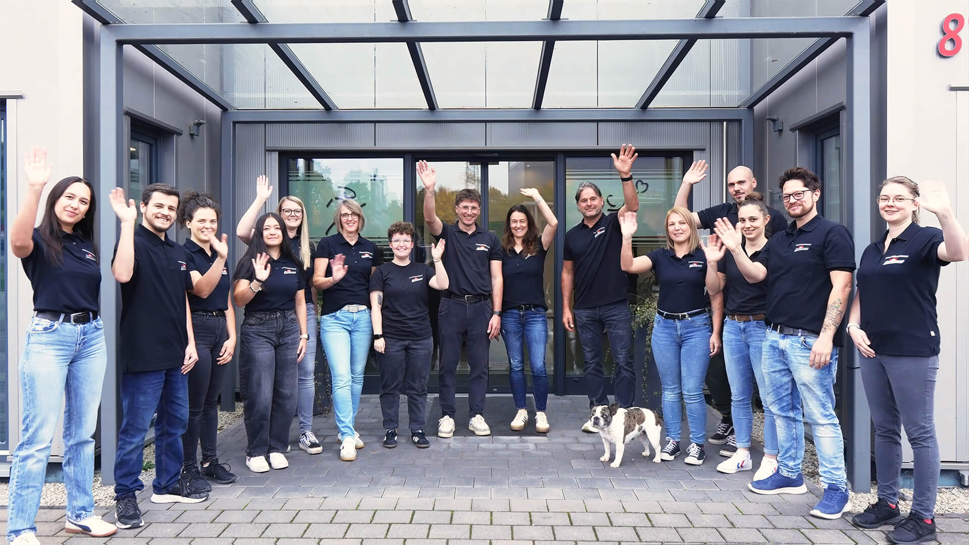 Team der Orthopädietechnik steht gemeinsam vor dem Firmengebäude und winken